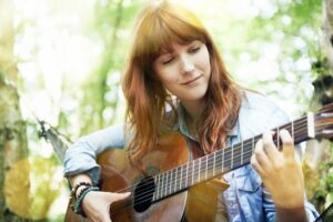 Red haired woman playing the guitar in the woods