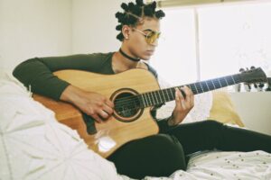 Young woman sitting in bed playing the guitar