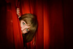 Woman peeking out from behind the stage curtains