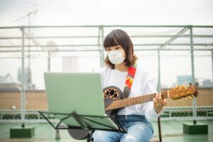 Masked woman taking an online guitar lesson