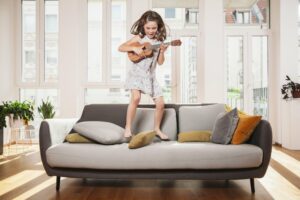 Little girl jumping on a couch playing ukulele