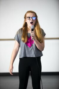 Little girl in glasses singing into a microphone