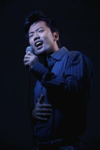 Asian man singing into a microphone 