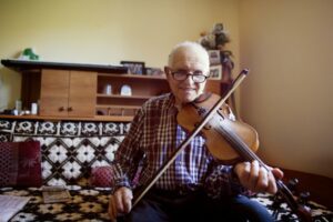 Elderly man playing the violin while sitting on a couch