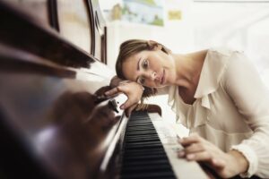 Woman leaning on piano looking down at the keys