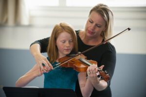 Woman showing music student how to hold her bow