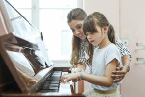 Woman showing little girl finger placement on piano