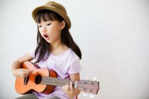 Little girl singing and playing ukulele