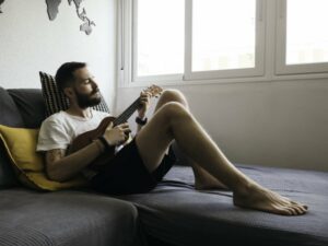 Young man relaxing on his couch playing ukulele