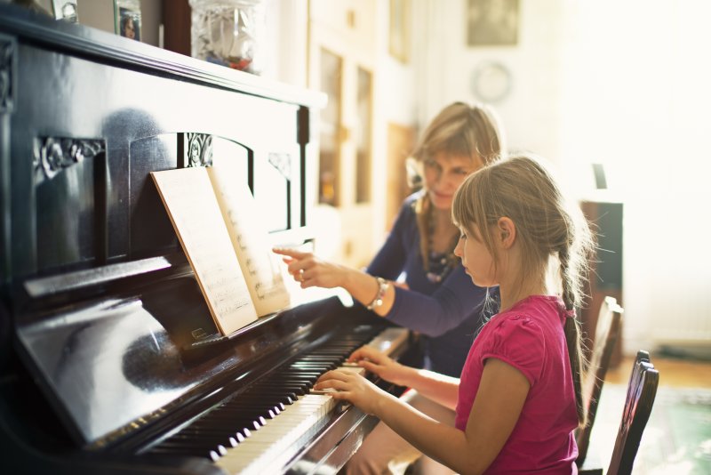 Mother teaching her daughter to play the piano in a sunny room