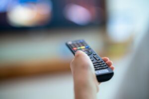 Close up of a man holding up a remote to a tv