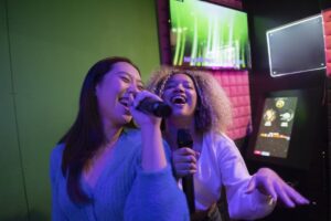 Two female friends singing karaoke in an arcade
