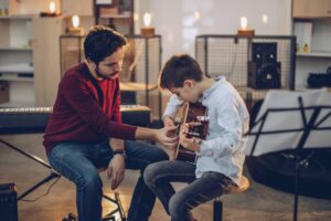 Man in red shirt teaching boy to play guitar
