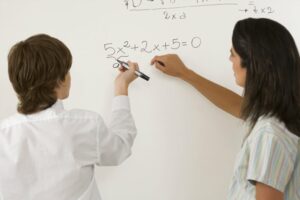 Teacher helping student solve quadratic equation on whiteboard