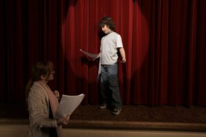 Boy on stage acting as drama teacher watches