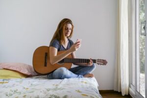Woman sitting on her bed with her guitar and cell phone