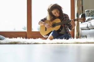 Young woman playing guitar sitting on the floor