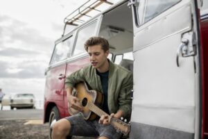 Young man playing an acoustic guitar in his van