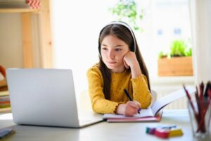 Little girl in a yellow shirt working with a writing tutor online 