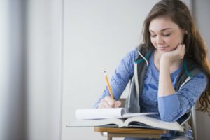 Teen girl in a blue shirt studying with a dreamy look on her face