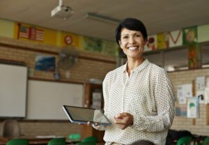 Smiling teacher standing in her class holding a tablet
