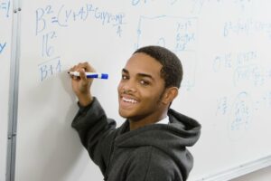 High school student smiling and writing an algebra problem on a white board