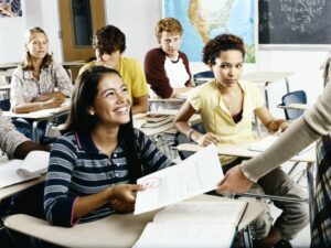 Student getting her homework back from the teacher as classmates look on